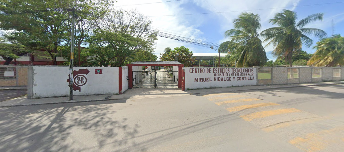 Fotografía en la que se muestra la entrada del plantel, conformada por dos muros blancos. En uno de los muros está escrito con letras grandes rojas CENTRO DE ESTUDIOS TECNOLÓGICOS INDUSTRIAL Y DE SERVICIO NÚMERO 82 MIGUEL HIDALGO Y COSTILLA. En medio de estos muros se encuentra la reja metálica que da acceso a las instalaciones. 